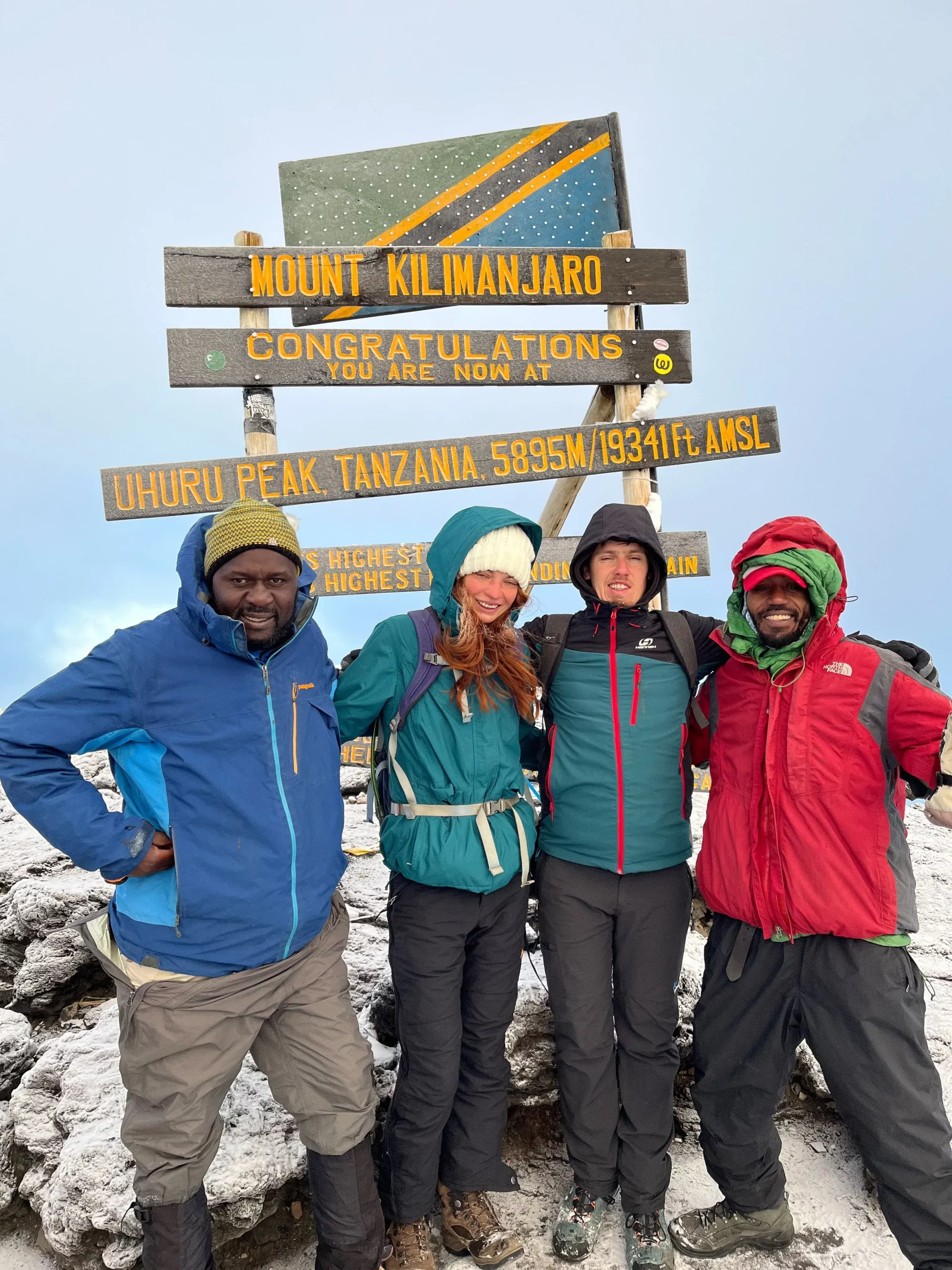 Our travelers who are a group of friends taking a picture with the Kilimanjaro summit at uhuru peak